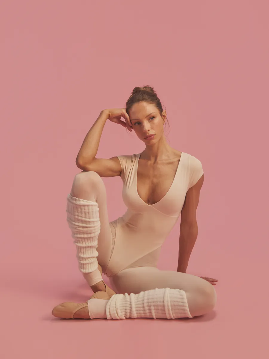 Jules seated on the floor in a blush bodysuit, chin resting on her hand
